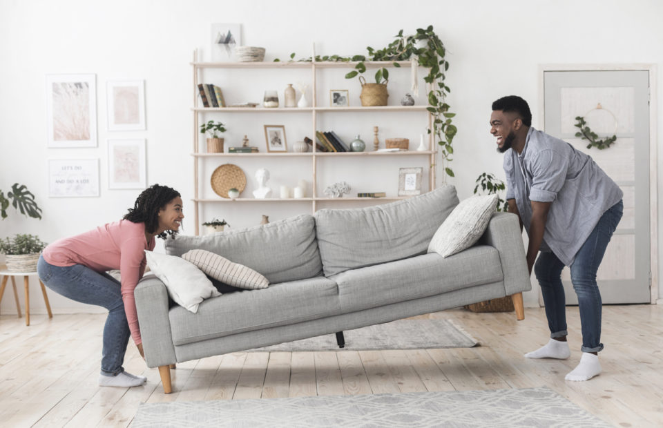 Couple moving sofa in living room, replacing furniture at home