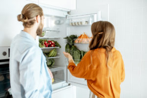 Couple choosing what to cook, taking fresh vegetables from the refrigerator at home