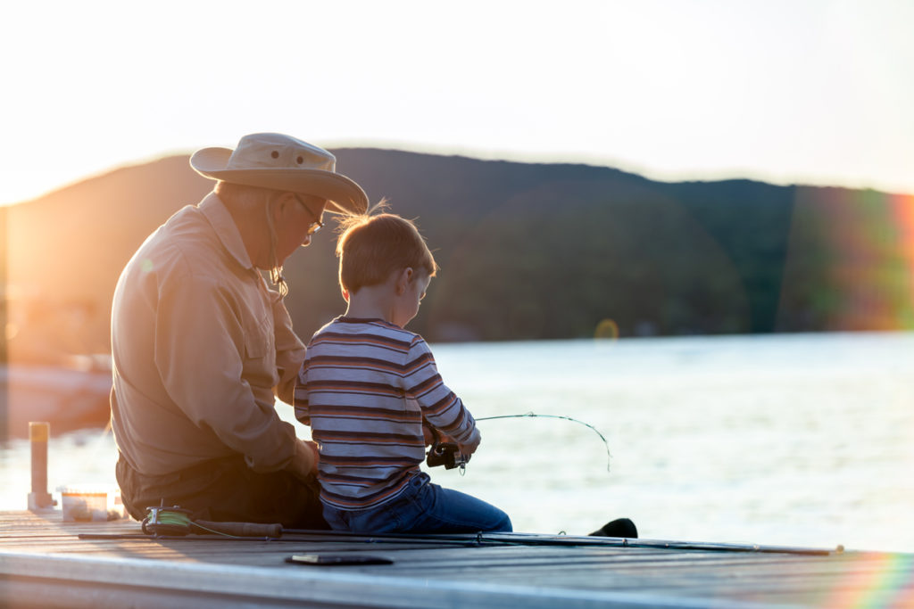 A grandfather is teaching his grandson to fish during sunset