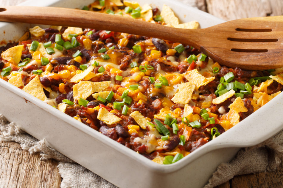 recipe for a delicious frito pie with ground beef, cheese, corn, beans and chips close-up in a baking dish on the table