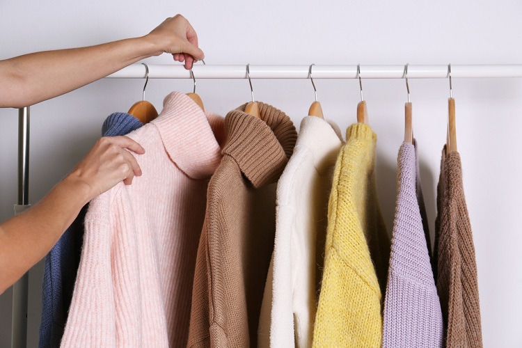Woman choosing sweater on rack against white background, closeup