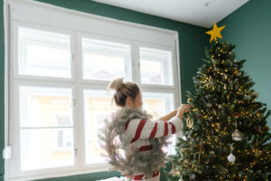 Photo of a young woman decorating Christmas tree at home.