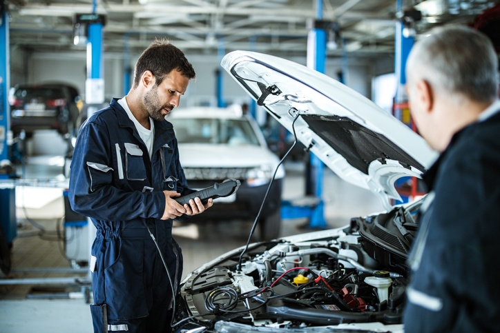 Young mechanic analyzing car's performance with diagnostic tool in a workshop.