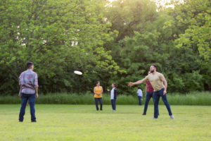 Brothers toss the frisbee around while the women in the family chat in the background.
